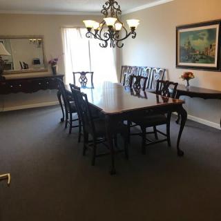 A dining room featuring a long table with chairs, illuminated by a central chandelier and complemented by wall art and a mirror.