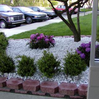 A landscaped garden featuring purple flowers and neatly arranged gravel, with parked cars in the background.