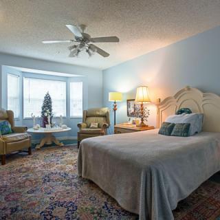 A cozy bedroom with a large bed, armchairs by the window, and a ceiling fan.