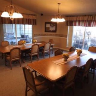 A warmly lit dining room featuring large tables and multiple chairs, with natural light streaming in through the windows.