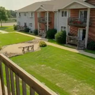 A view from the balcony overlooking a neatly maintained green lawn and an apartment complex with outdoor seating area.