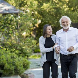 An elderly couple enjoys a walk together in a lush garden setting.