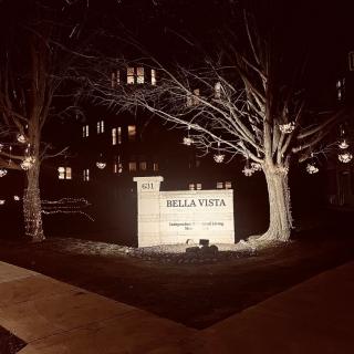 A nighttime view of an illuminated sign and trees with hanging lights in front of a building.