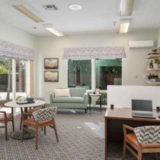A modern office space featuring desks, a sofa, chairs, and large windows.