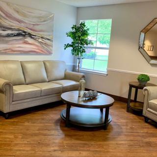 A cozy living room with a beige sofa set, round coffee table, wall art, indoor plant, and a decorative mirror.