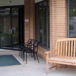A building entrance with a wooden bench and metal chairs outside.