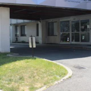 The image shows an entrance to a building with a covered driveway leading to glass doors.