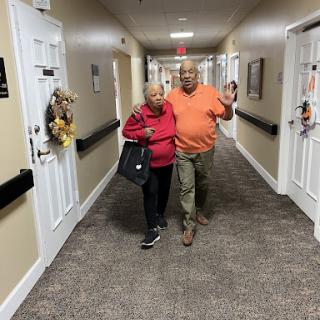 An elderly couple enjoying a walk together in a community hallway.