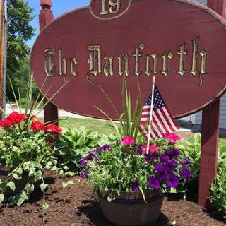 A garden display featuring a sign reading 'The Danforth', surrounded by colorful flowers and a small American flag, on a sunny day.
