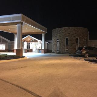 A well-lit building entrance at night with a parked car nearby.