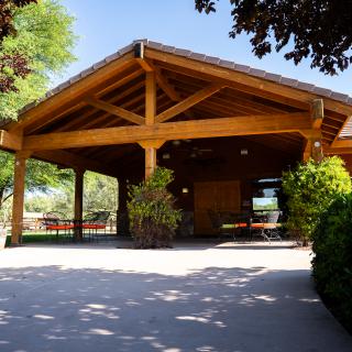 A wooden pergola providing shade in a garden setting, surrounded by trees and greenery.