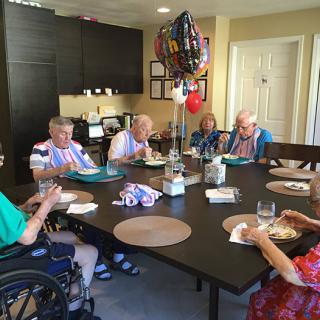 A group of seniors enjoying a meal together around a table with decorative balloons.