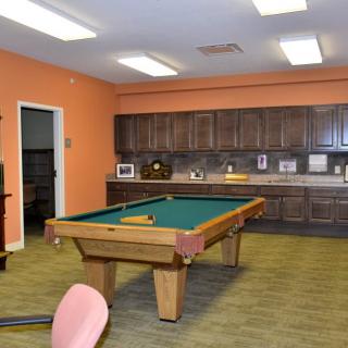 A game room featuring a pool table and a kitchen area with orange walls.