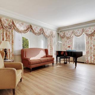 A traditional living room featuring a grand piano, a couch, an armchair, and elegant curtains.