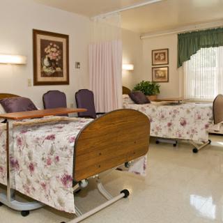 A well-maintained patient room in a medical facility, featuring floral-patterned bedding and comfortable seating.