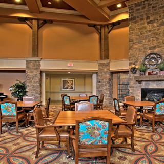 A cozy dining area with wooden tables and colorful chairs, featuring a stone fireplace and high ceilings.