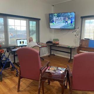 A cozy common area in an elderly care facility, featuring a TV, computer station, and comfortable seating.