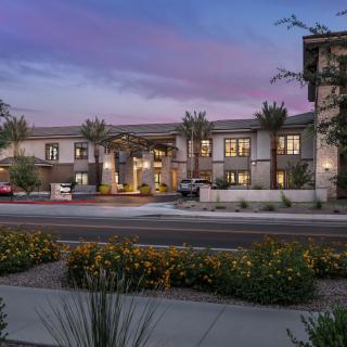 An illuminated building surrounded by landscaping at dusk, under a colorful sky.