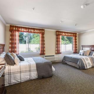 A spacious bedroom with two neatly made beds, large windows, and patterned curtains.