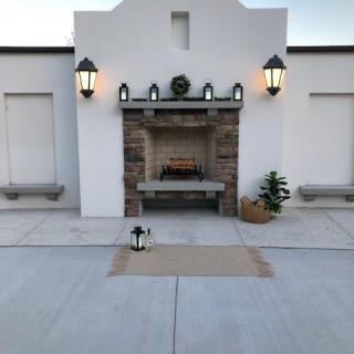 An elegant outdoor patio with a central fireplace, flanked by lanterns and simple decor.