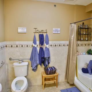 A neatly organized bathroom with blue towels hanging on the wall, a toilet, and a bathtub with a shower curtain.