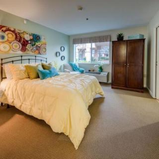 A cozy bedroom with a large bed, colorful pillows, abstract art on the wall, and a wooden wardrobe.