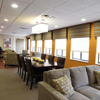 A spacious and modern interior featuring a comfortable living area with a sofa and a dining table, complemented by natural light from large windows.