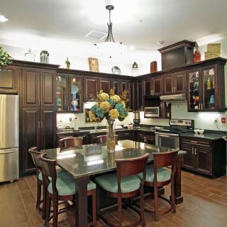 A modern kitchen with dark wood cabinets, featuring a central island and chandelier lighting.