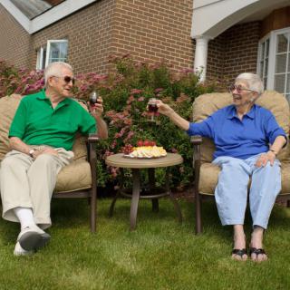 An elderly couple enjoying a toast while sitting outdoors in their garden.