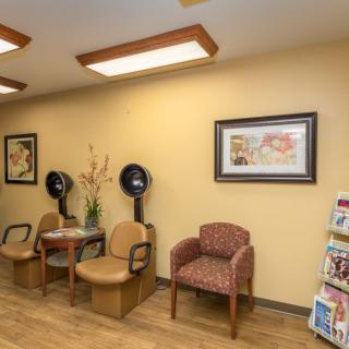 A cozy waiting room with chairs, brochures, and salon equipment against a warmly painted wall.
