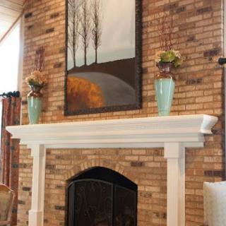 A cozy fireplace with a white mantel, adorned with vases and a landscape painting, set against a brick wall.