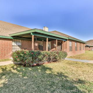 A brick suburban house with a green porch and a well-maintained lawn.