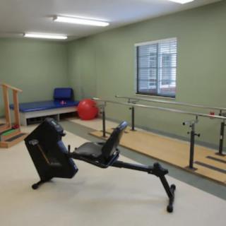 A rehabilitation room with exercise equipment, including parallel bars and a recumbent bike.