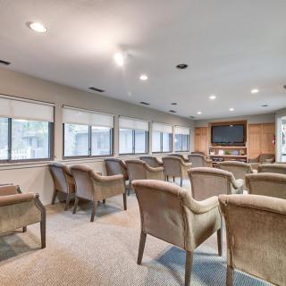 A spacious conference room with rows of chairs facing a large screen and windows providing natural light.