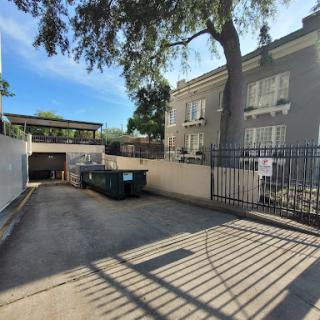 A serene outdoor view of a building's parking area, featuring garbage bins and a tree casting shadows.