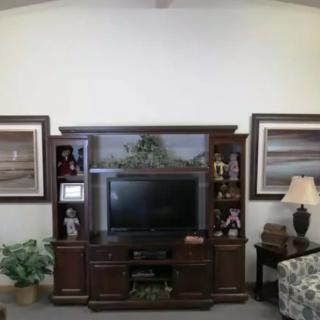 A cozy living room setup featuring a large entertainment center with a television, surrounded by framed artwork and home decor items.
