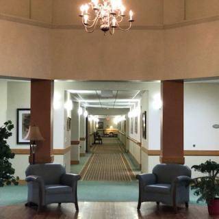 A well-lit hallway with two chairs under a chandelier.