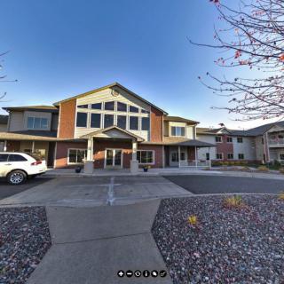 A two-story building with a large entrance and a driveway, adjacent to parked vehicles under a clear blue sky.