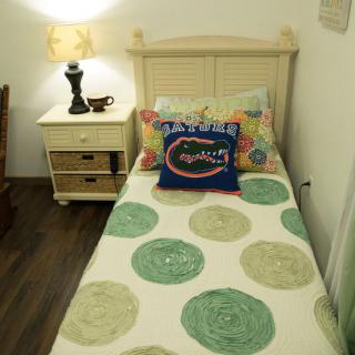 A cozy bedroom with a single bed, colorful pillows, and a nightstand with a lamp.