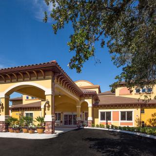 A sunny view of a building's entrance with Mediterranean-style architecture and surrounding landscaping.
