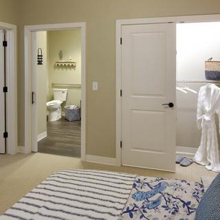 A cozy bedroom with a view of the bathroom and closet area, featuring neutral tones and striped bedding.