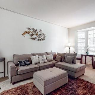 A cozy living room with a sectional sofa, ottoman, and decorative wall art.