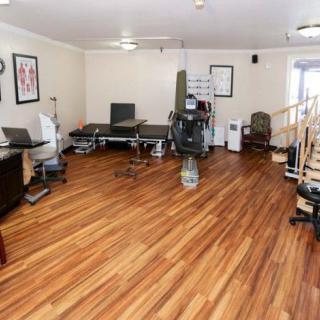 A spacious physical therapy room featuring exercise equipment and treatment tables on a wooden floor.