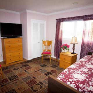 A cozy bedroom featuring a floral bedspread, wooden furniture, and a television.