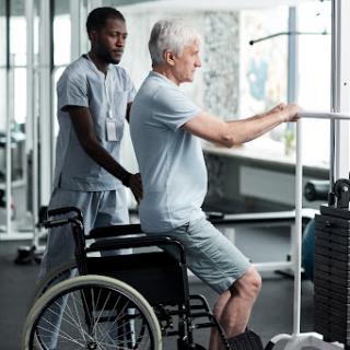 A caregiver assisting an elderly person in a wheelchair with exercise in a gym setting.