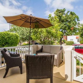 A cozy patio setup with wicker furniture and a sun umbrella, surrounded by greenery.