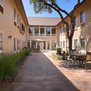 A peaceful courtyard with outdoor seating and a path lined by buildings under a clear blue sky.