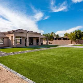 A modern residential house with a large, well-maintained lawn under a clear blue sky.
