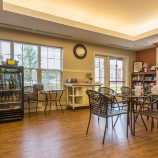 A cozy cafe interior with tables and chairs, featuring large windows that let in natural light.