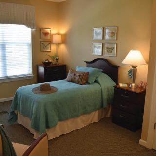 A cozy bedroom with a single bed, adorned with a turquoise bedspread and illuminated by soft lighting from lamps.